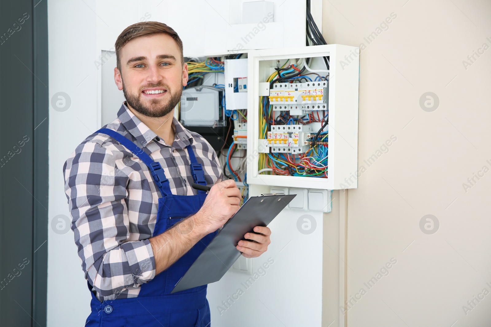 Photo of Male electrician with clipboard near fuse board indoors, space for text