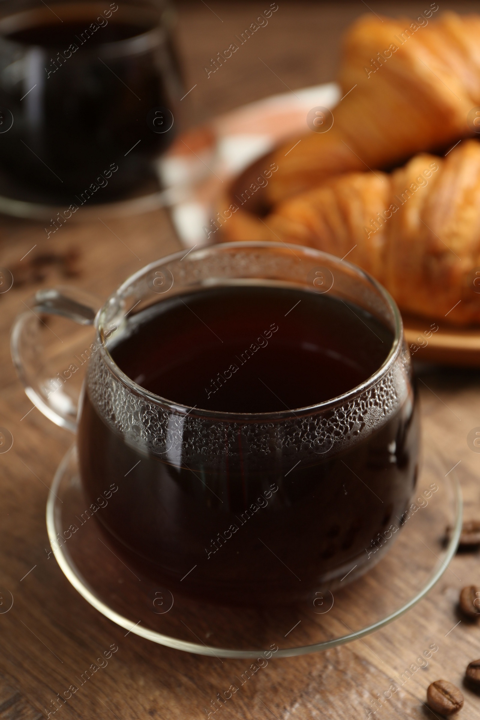 Photo of Hot coffee in glass cup and beans on wooden table, closeup