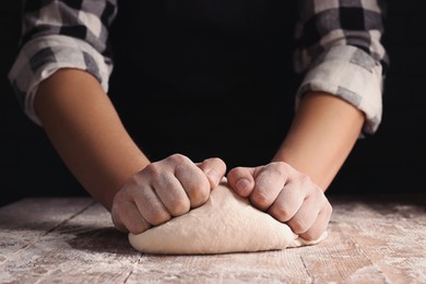 Man kneading dough at wooden table on dark background, closeup