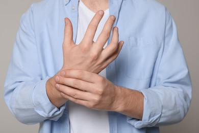 Photo of Man suffering from pain in his hand on light grey background, closeup. Arthritis symptoms