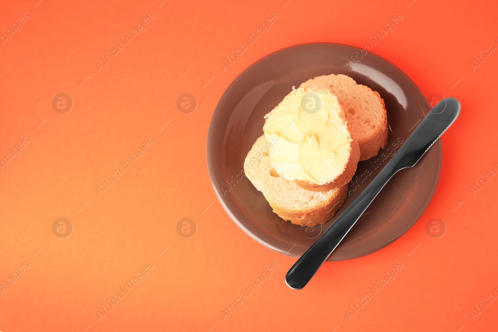 Photo of Slices of delicious baguette with butter and knife on orange background. Space for text