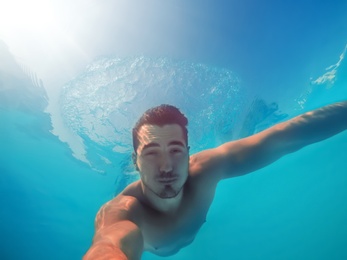 Photo of Handsome young man swimming in pool, underwater view