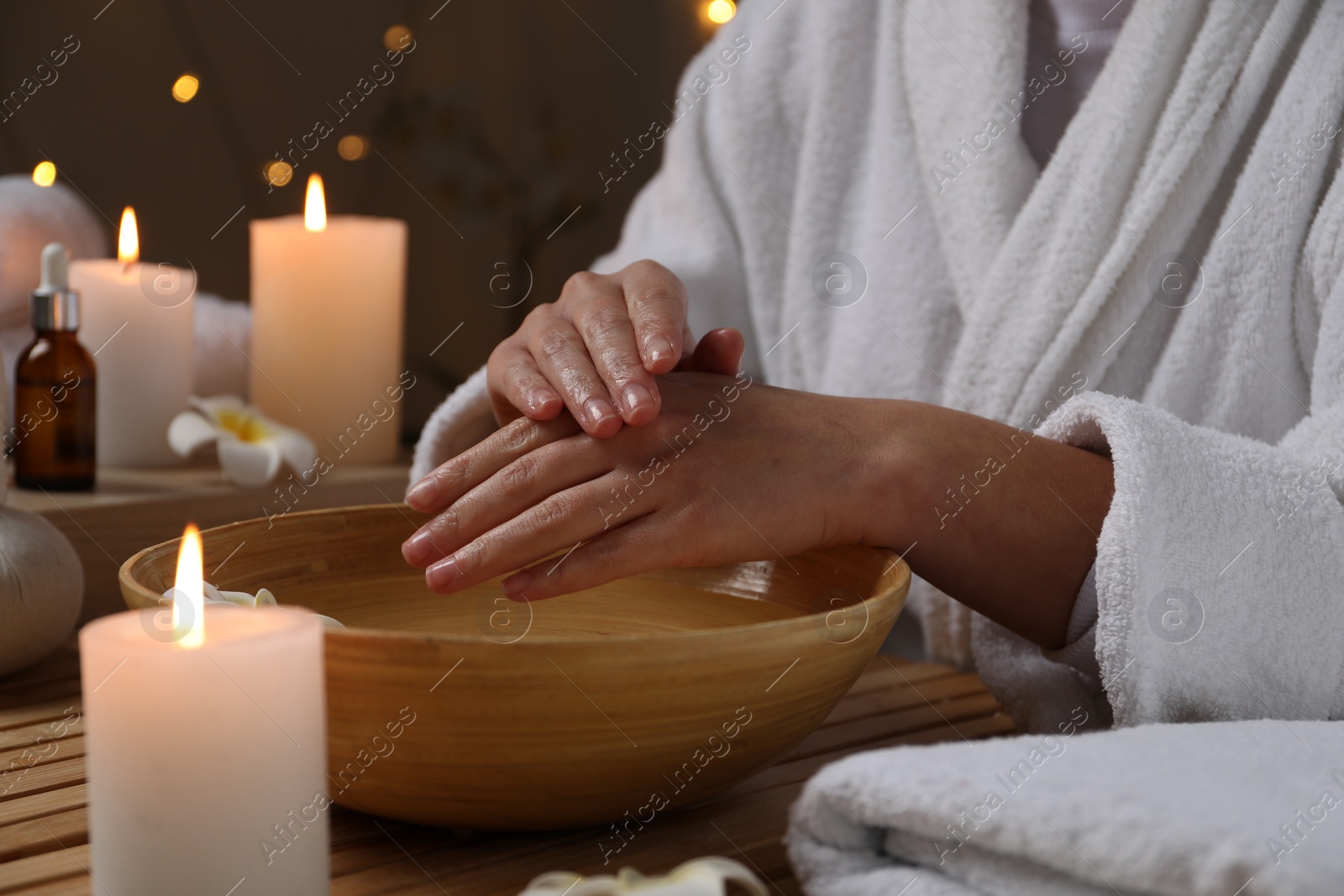 Photo of Woman soaking her hands in bowl of water at table, closeup. Spa treatment