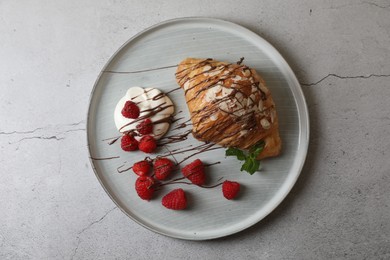 Photo of Delicious croissant with raspberries, cream and chocolate on grey table, top view