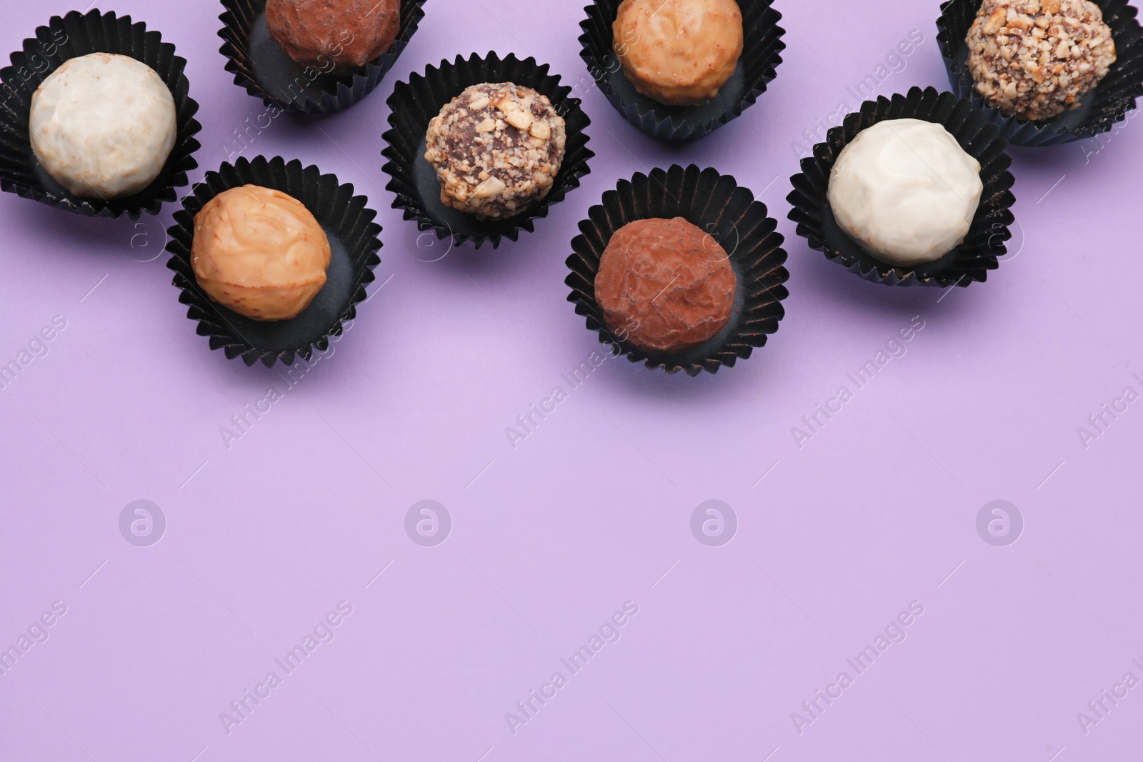 Photo of Tasty chocolate candies on violet background, flat lay. Space for text