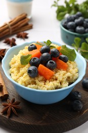 Photo of Tasty millet porridge with blueberries, pumpkin and mint in bowl on white table, closeup