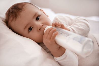 Photo of Cute little baby with bottle lying in comfortable crib. Bedtime