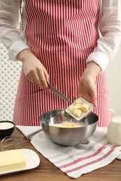 Photo of Woman adding fresh butter into bowl with flour at wooden table, closeup