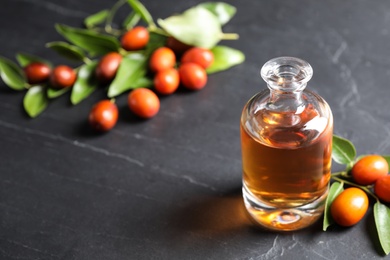 Photo of Glass bottle with jojoba oil and seeds on grey stone table. Space for text