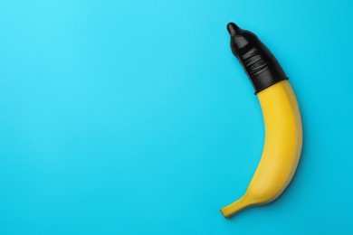 Photo of Banana with condom on light blue background, top view and space for text. Safe sex concept