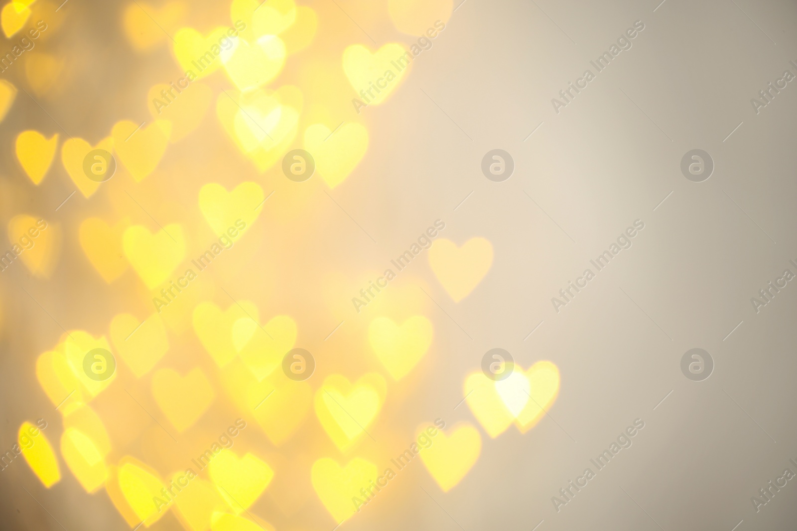 Photo of Blurred view of gold heart shaped lights on light background