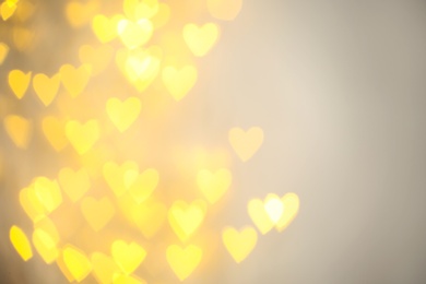 Photo of Blurred view of gold heart shaped lights on light background