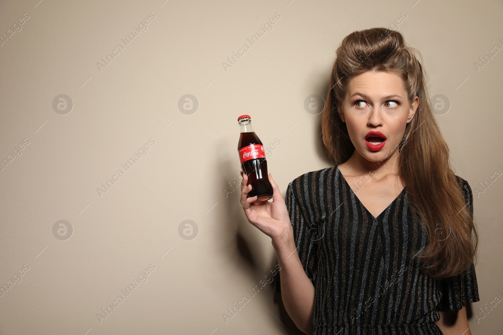 Photo of MYKOLAIV, UKRAINE - NOVEMBER 28, 2018: Young woman with bottle of Coca-Cola on color background, space for text