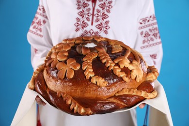 Photo of Woman with korovai on light blue background, closeup. Ukrainian bread and salt welcoming tradition