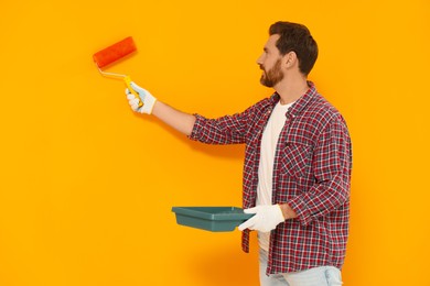 Photo of Designer painting orange wall with dye roller
