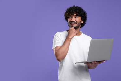 Smiling man with laptop on purple background, space for text