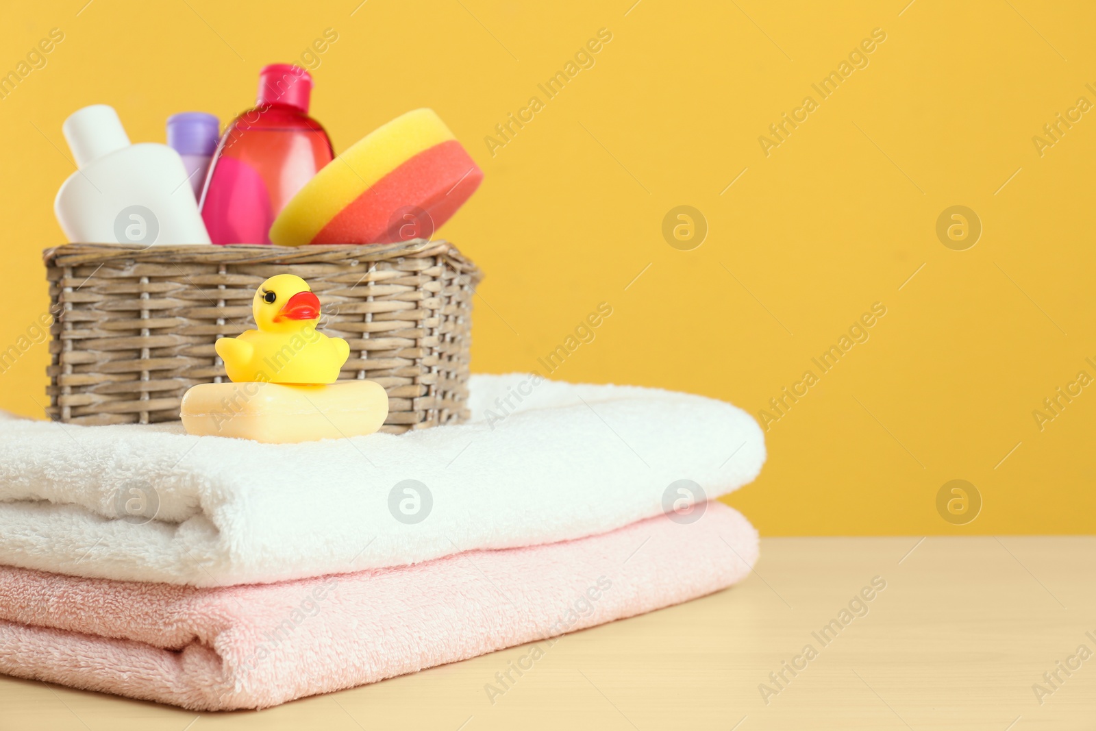 Photo of Wicker basket with baby cosmetic products, toy and towels on table against color background. Space for text