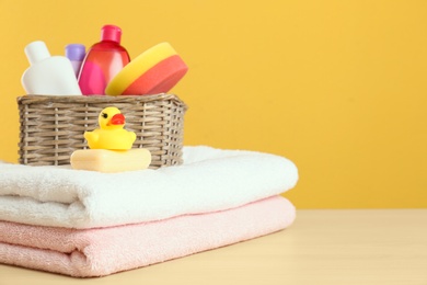 Photo of Wicker basket with baby cosmetic products, toy and towels on table against color background. Space for text