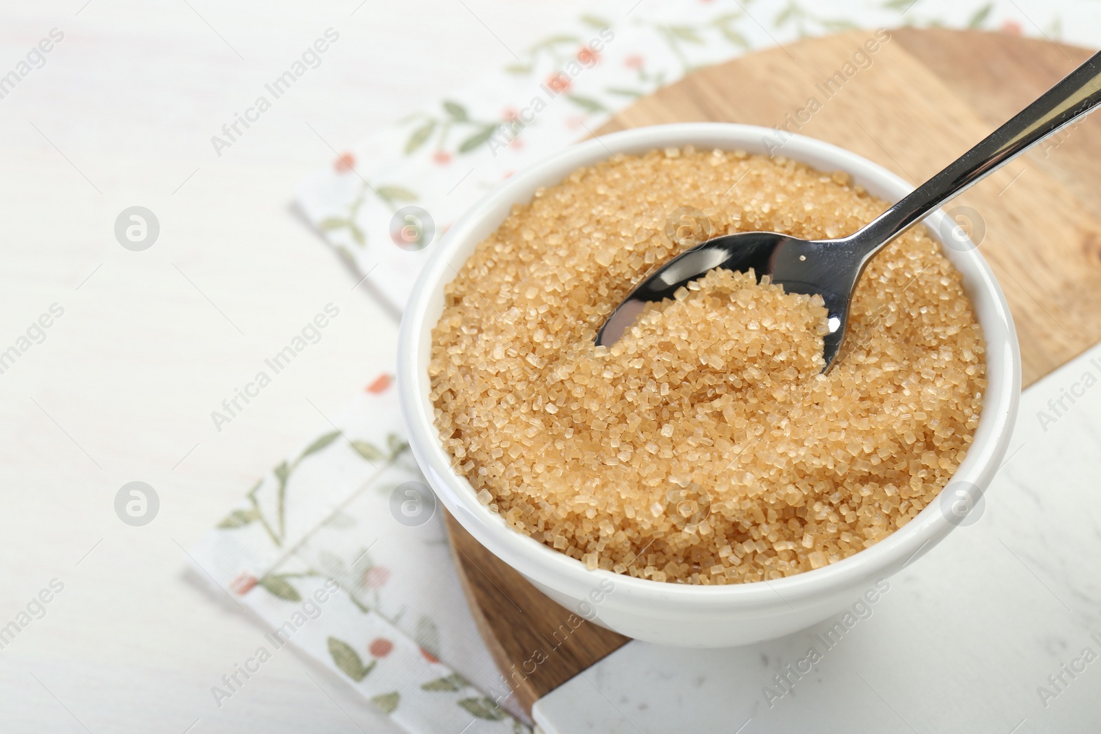 Photo of Brown sugar in bowl and spoon on white table, closeup. Space for text