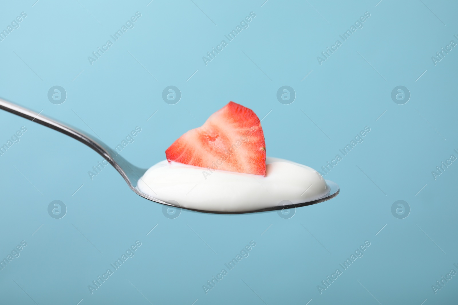 Photo of Delicious natural yogurt with fresh strawberry in spoon on light blue background