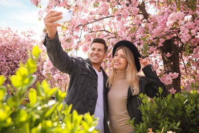 Happy couple taking selfie near blossoming sakura outdoors on spring day