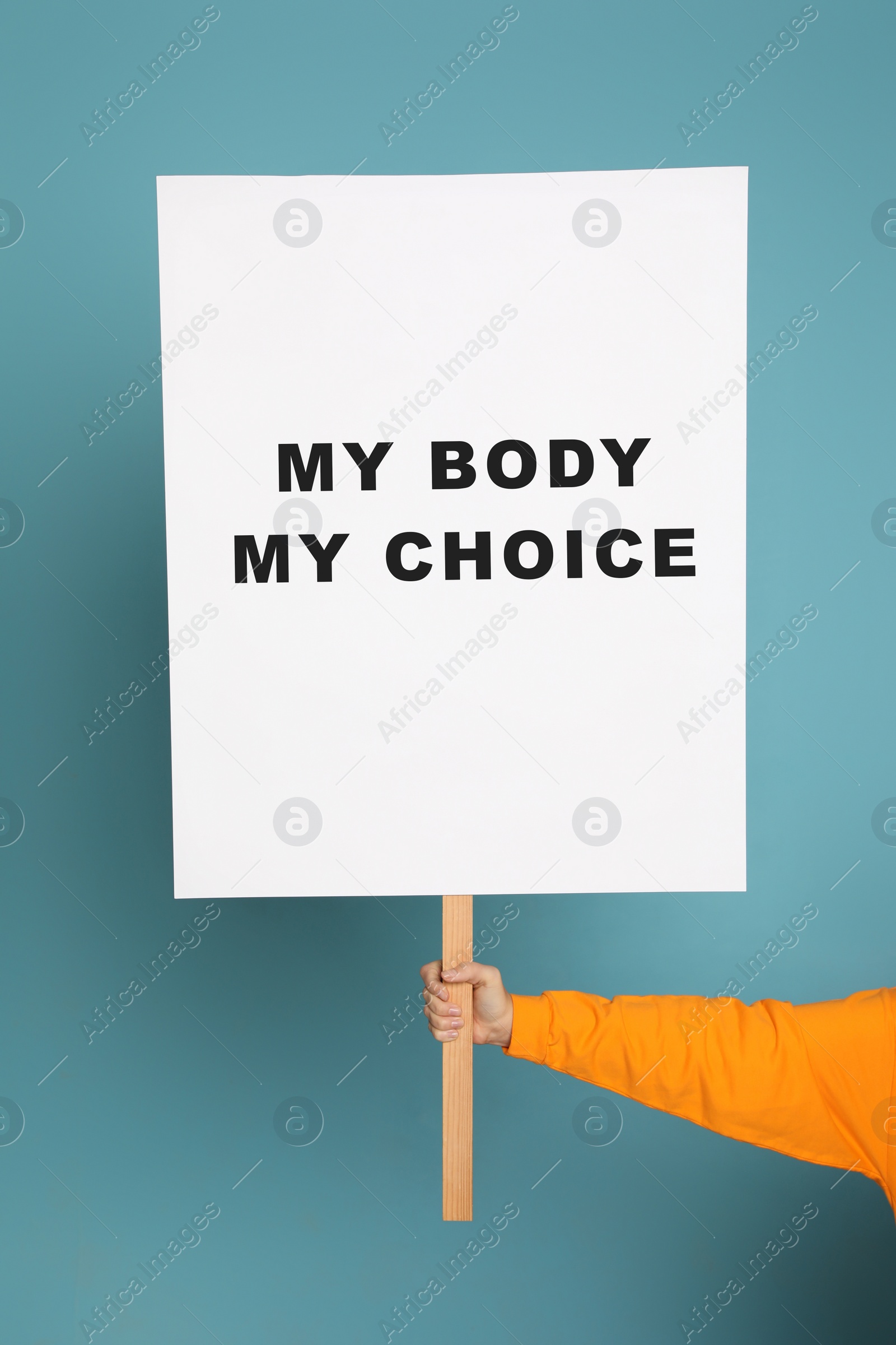 Image of Woman holding placard with phrase My Body My Choice on light blue background, closeup. Abortion protest