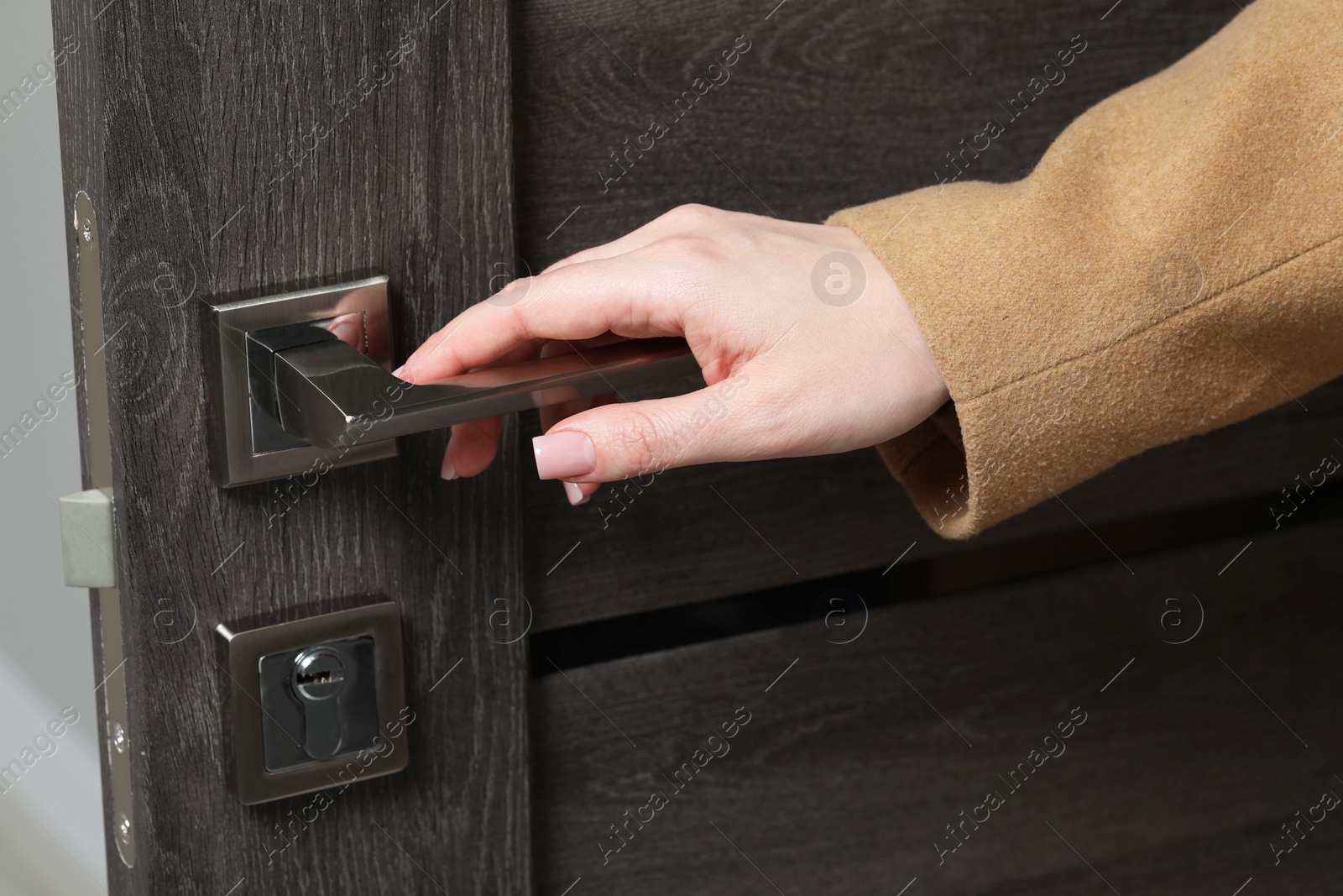 Photo of Woman opening wooden door indoors, closeup of hand on handle