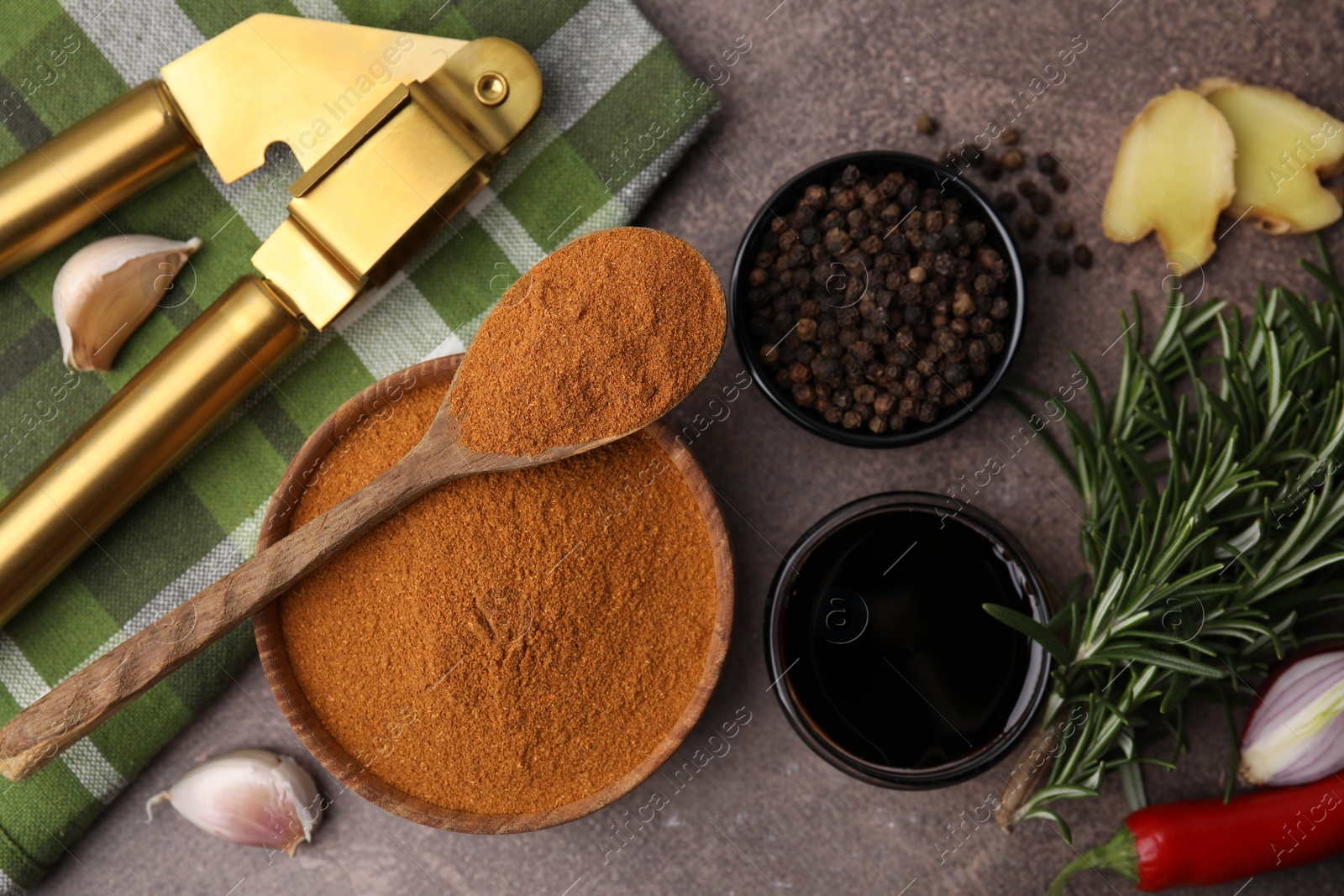 Photo of Aromatic spices, fresh ingredients for marinade and garlic press on brown table, flat lay