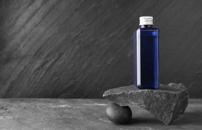 Photo of Bottle of cosmetic product and stones on light grey background. Space for text