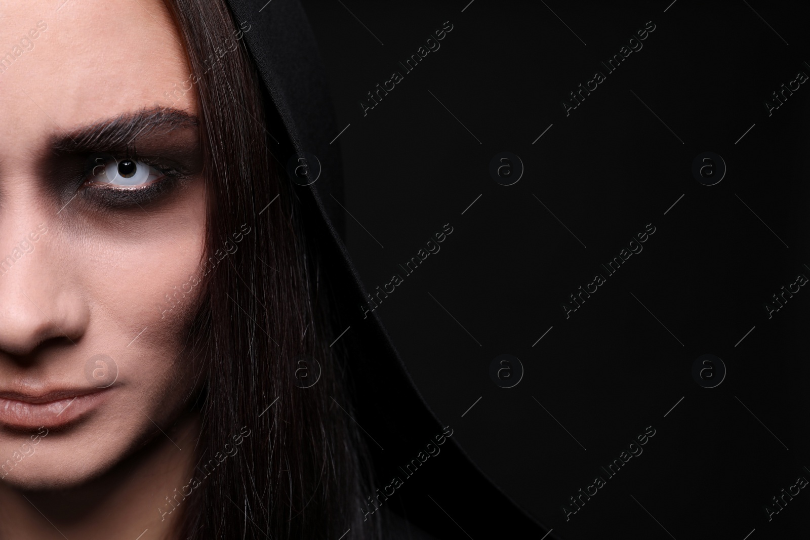 Photo of Mysterious witch with spooky eyes on black background, closeup. Space for text