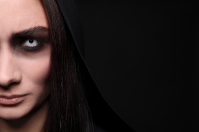 Photo of Mysterious witch with spooky eyes on black background, closeup. Space for text