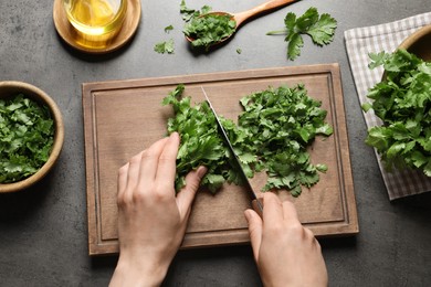 Photo of Woman cutting fresh green cilantro at grey table, top view