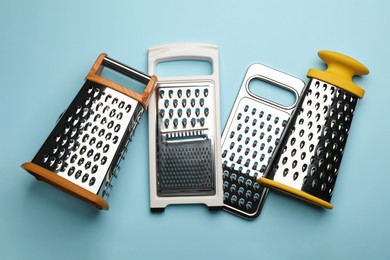 Different modern graters on light blue background, flat lay