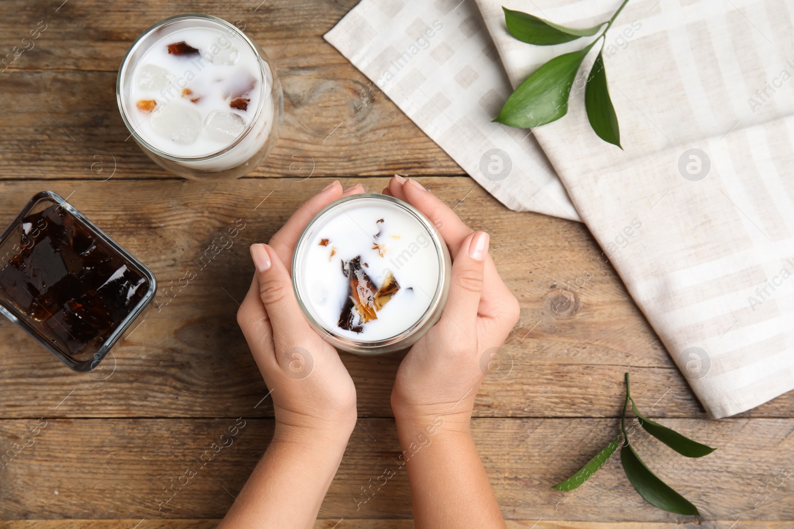 Photo of Woman holding glass of milk with delicious grass jelly at wooden table, top view