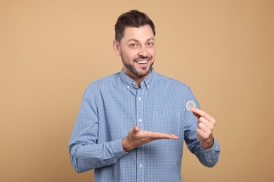 Happy man holding condom on beige background, closeup