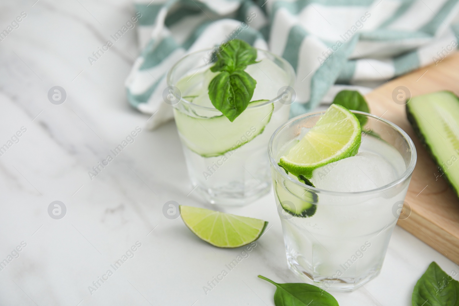 Photo of Tasty fresh cucumber water with sliced lime and basil on white marble table, space for text