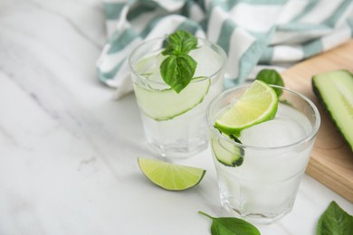 Tasty fresh cucumber water with sliced lime and basil on white marble table, space for text