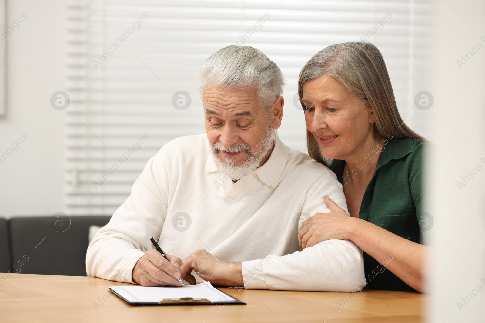 Photo of Senior couple signing Last Will and Testament indoors