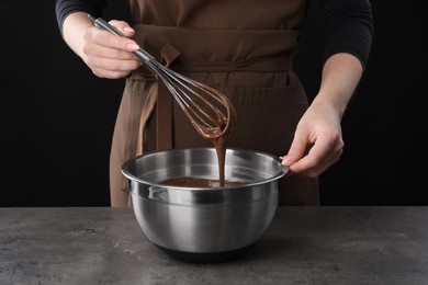 Woman with whisk mixing chocolate cream at grey table against black background, closeup