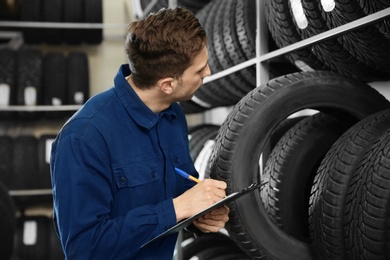 Photo of Young male mechanic with clipboard near tires in automobile service center