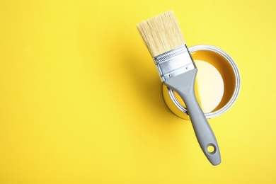 Paint can and brush on yellow background, top view. Space for text