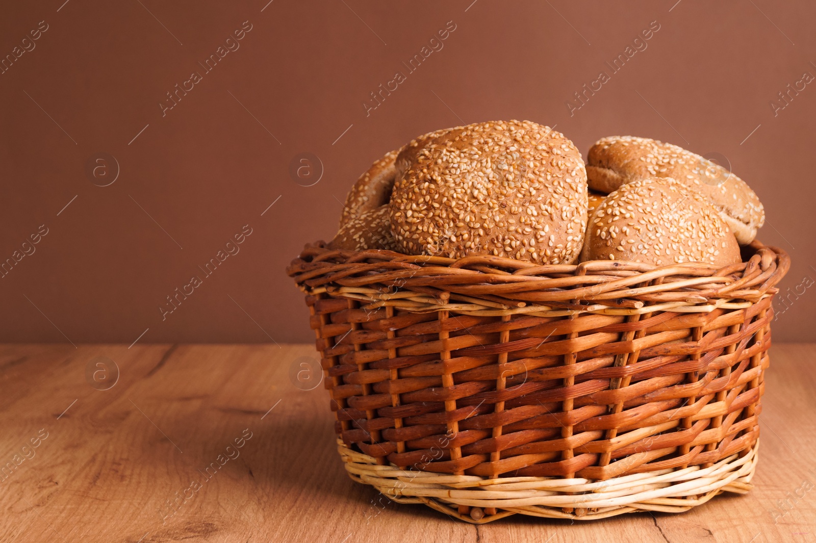 Photo of Wicker basket of fresh buns with sesame seeds on wooden table. Space for text