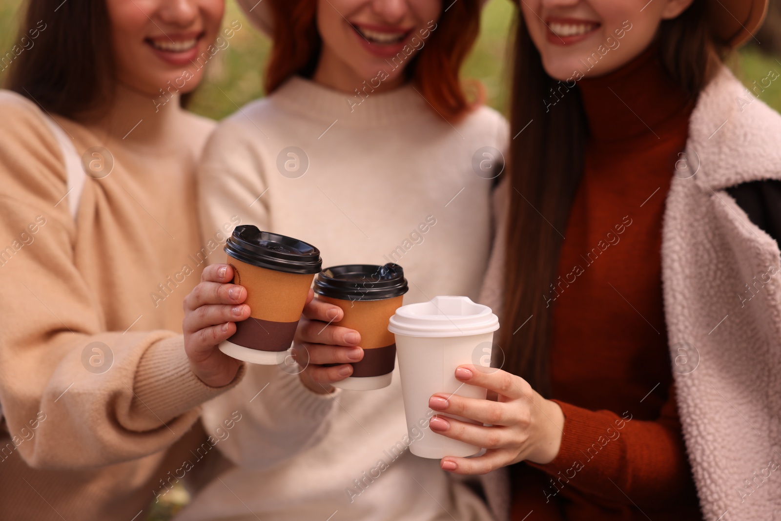 Photo of Happy three friends with cups of coffee outdoors, closeup