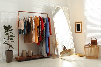 Rack with different stylish women's clothes and mirror indoors