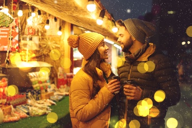 Image of Lovely couple with cups of hot drinks spending time together at Christmas fair