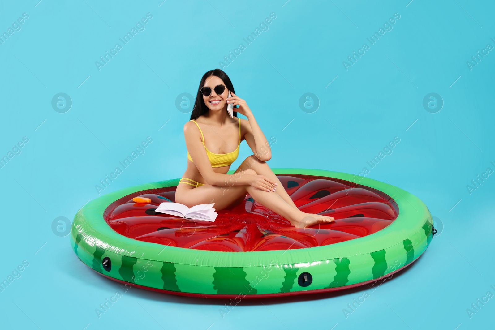 Photo of Young woman in stylish sunglasses on inflatable mattress against light blue background