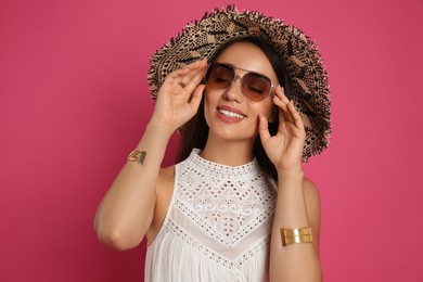 Photo of Beautiful young woman with straw hat and sunglasses on crimson background. Stylish headdress