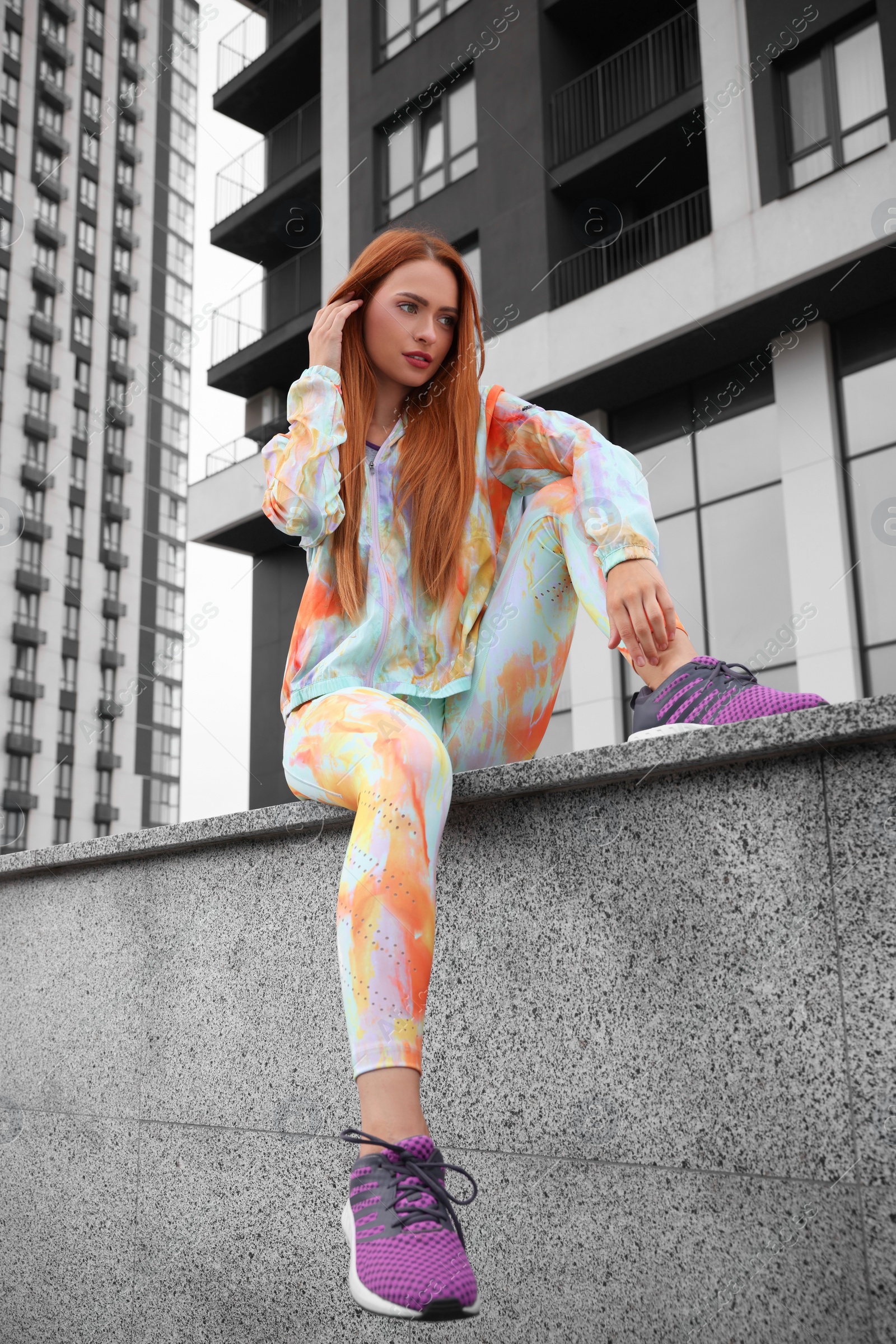 Photo of Beautiful woman in gym clothes sitting on parapet on street, low angle view