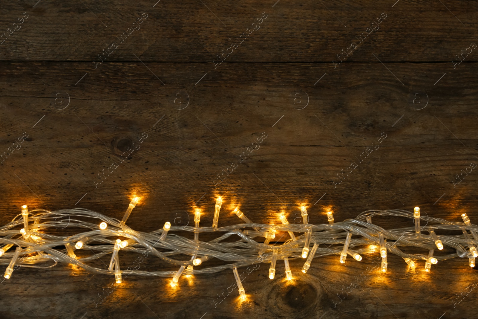 Photo of Glowing Christmas lights on wooden background, top view. Space for text