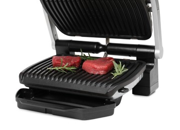 Photo of Electric grill with raw meat steaks and rosemary isolated on white